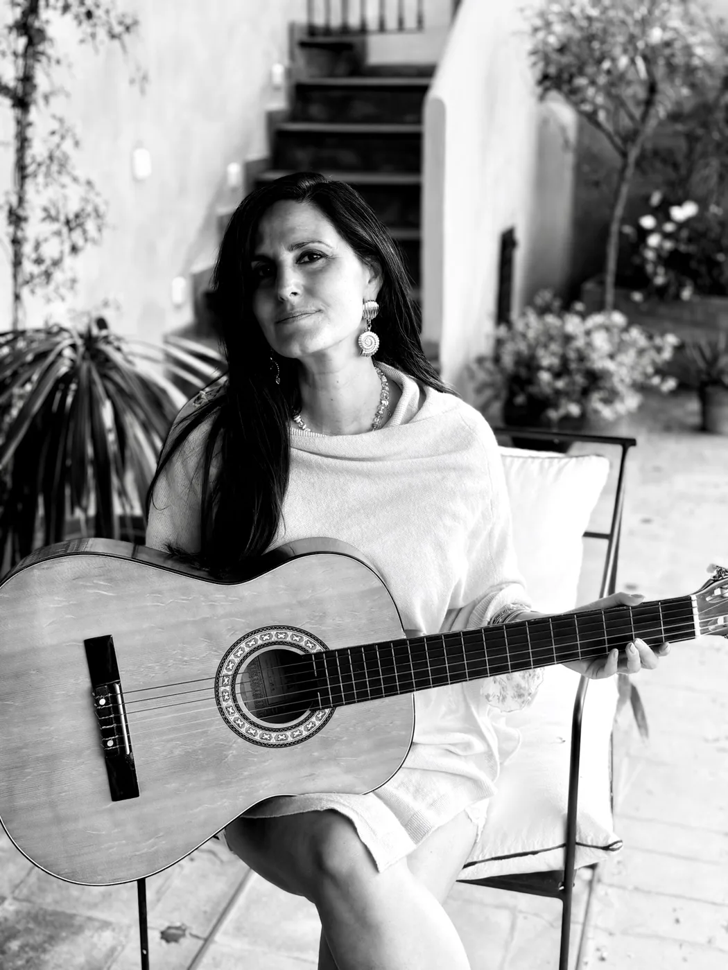 Deborah Rose sitting in a courtyard with an acoustic guitar, in black and white